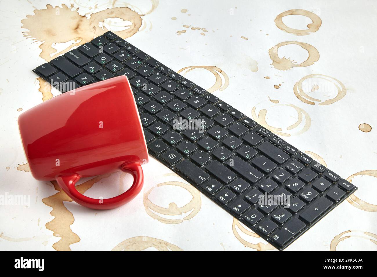 Tasse de café rouge renversée sur un clavier d'ordinateur sur une table avec des taches de café. Clavier rempli de boisson au café Banque D'Images