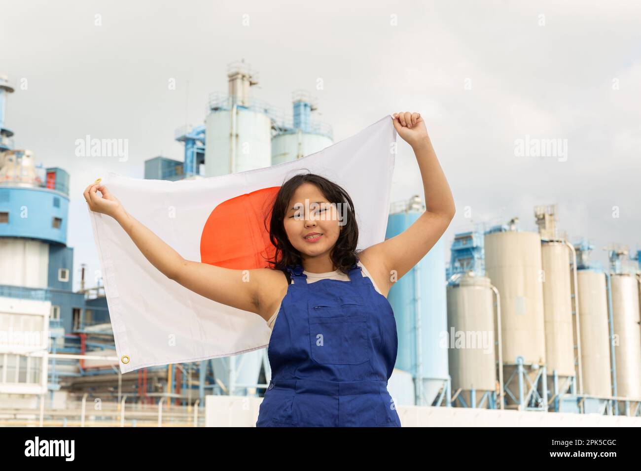 Jeune femme heureuse avec drapeau du Japon contre fond d'usine Banque D'Images