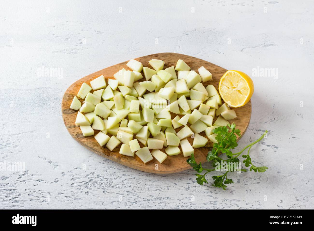 Planche en bois avec des tranches de pomme coupées pour salade, arrosées de jus de citron, d'un demi-citron et d'une branche de persil sur fond bleu clair, vue du dessus. Cuisine Banque D'Images