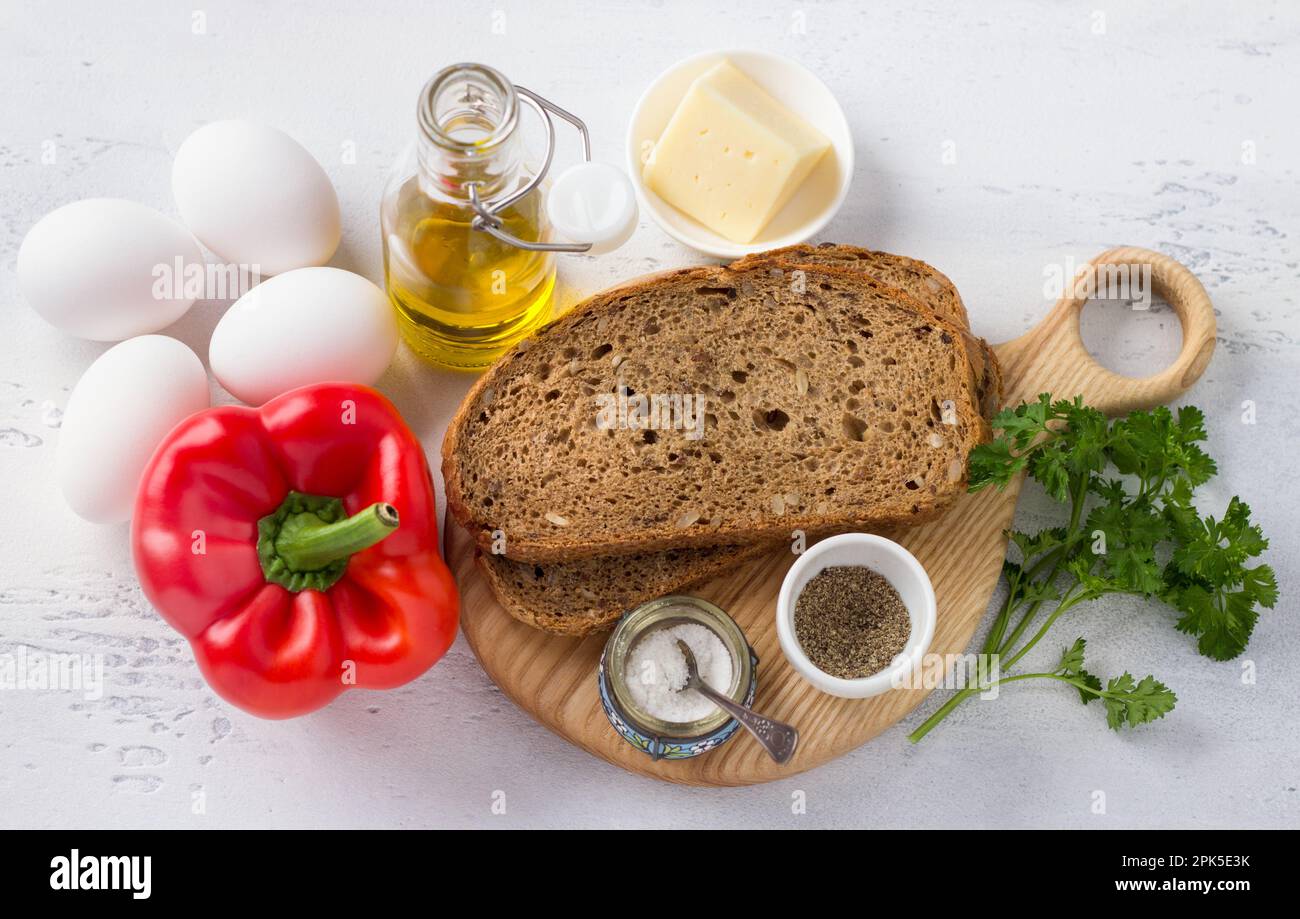 Ingrédients pour de délicieux oeufs brouillés: Pain de levain de seigle aux graines, oeufs, poivre rouge doux, huile d'olive, fromage dur, herbes, sel et poivre sur un Banque D'Images