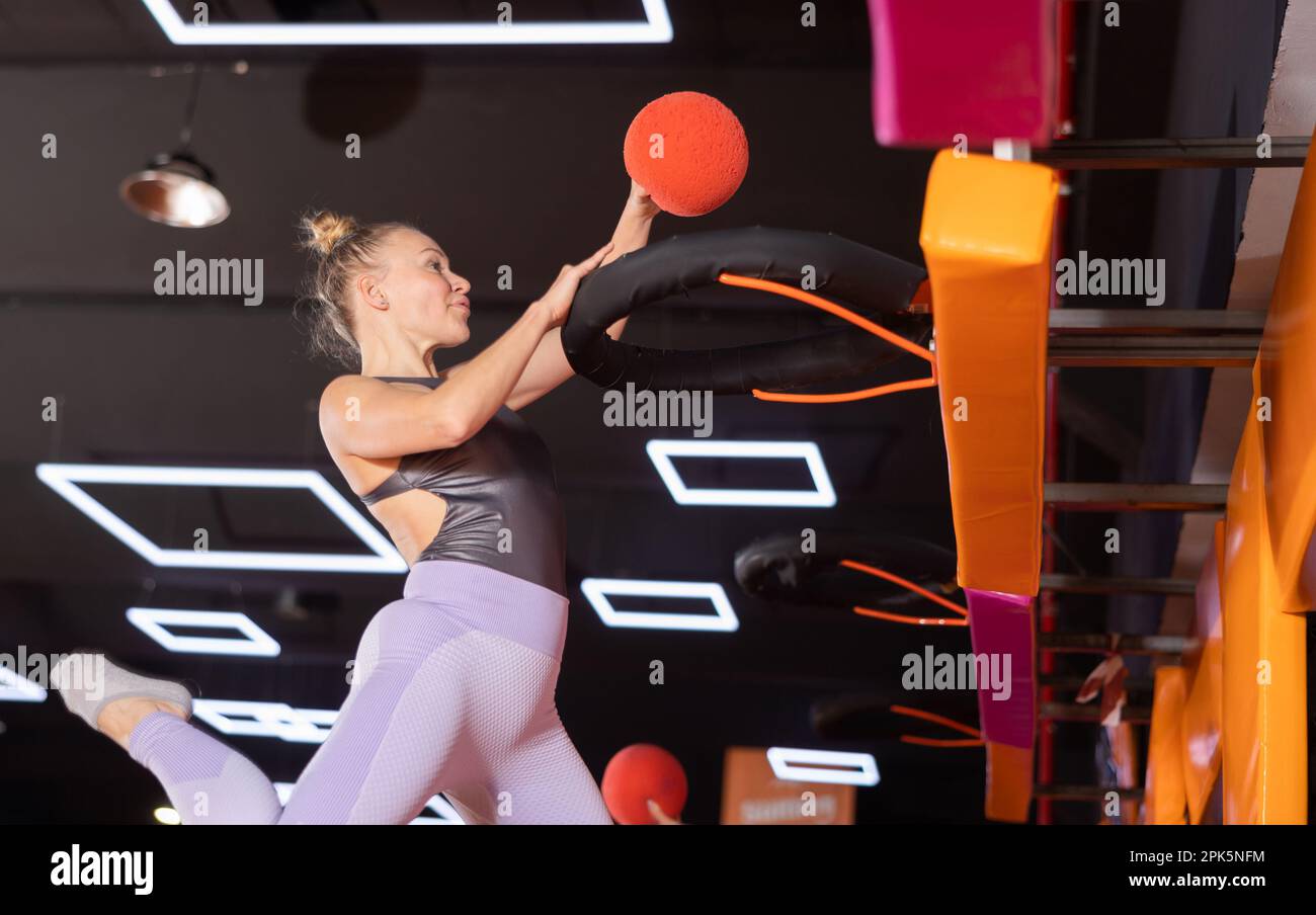 Femme européenne active dans des vêtements de sport jouant au basket-ball tout en rebondissant sur des trampolines colorés à l'intérieur dans le centre de sports de loisirs Banque D'Images