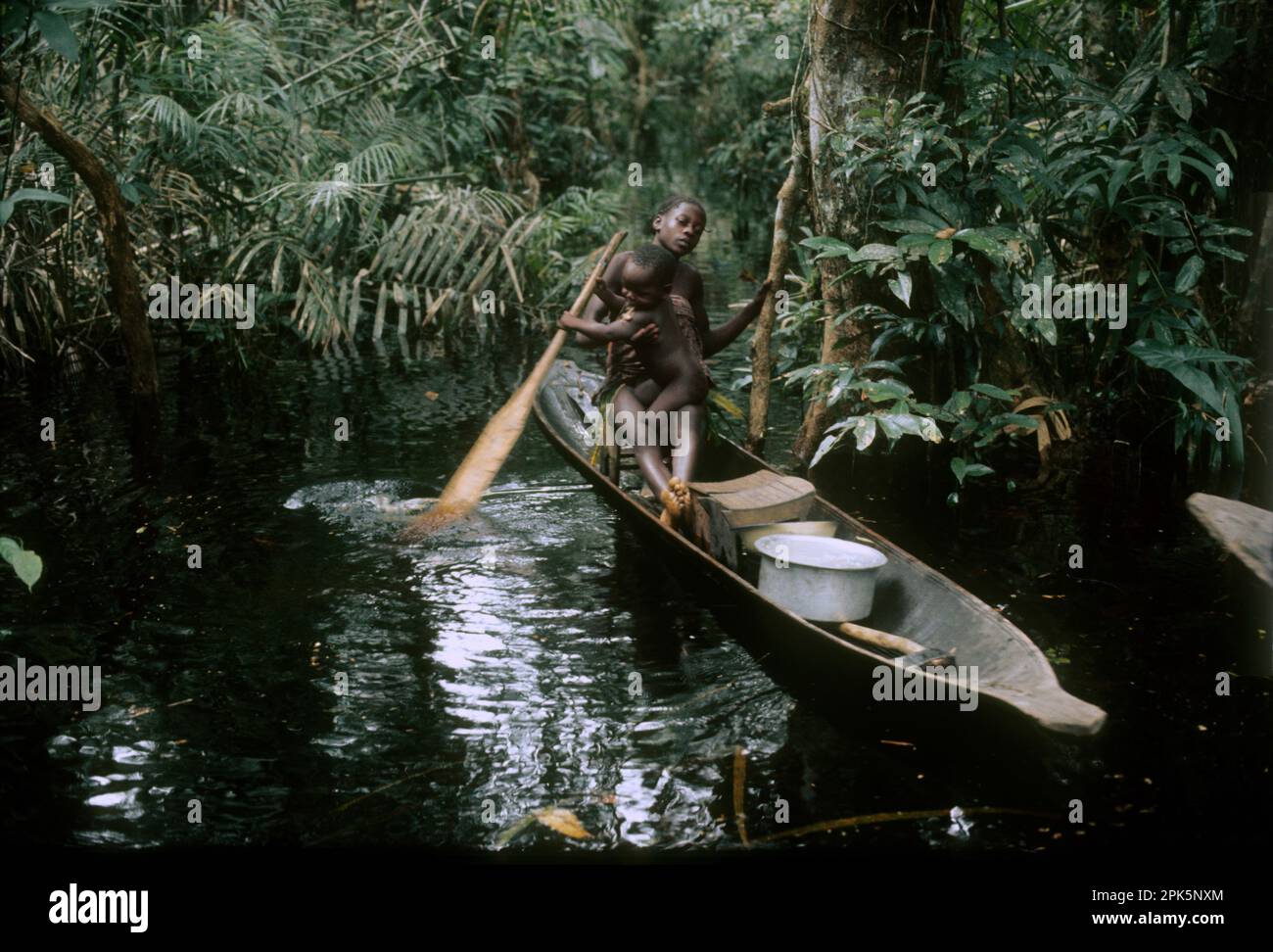 Afrique, République démocratique du Congo, région des îles de la rivière Ngiri, groupe ethnique Libinza : fille avec bébé apprenant à pagayer en canoë dans la forêt marécageuse. Banque D'Images