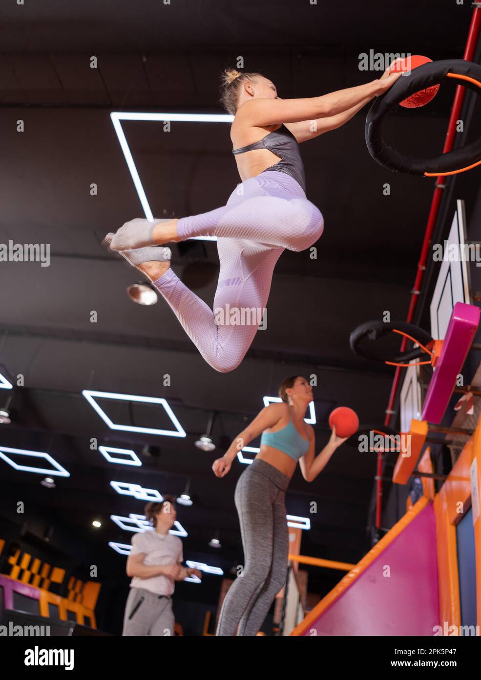 Femme européenne active dans des vêtements de sport jouant au basket-ball tout en rebondissant sur des trampolines colorés à l'intérieur dans le centre de sports de loisirs Banque D'Images