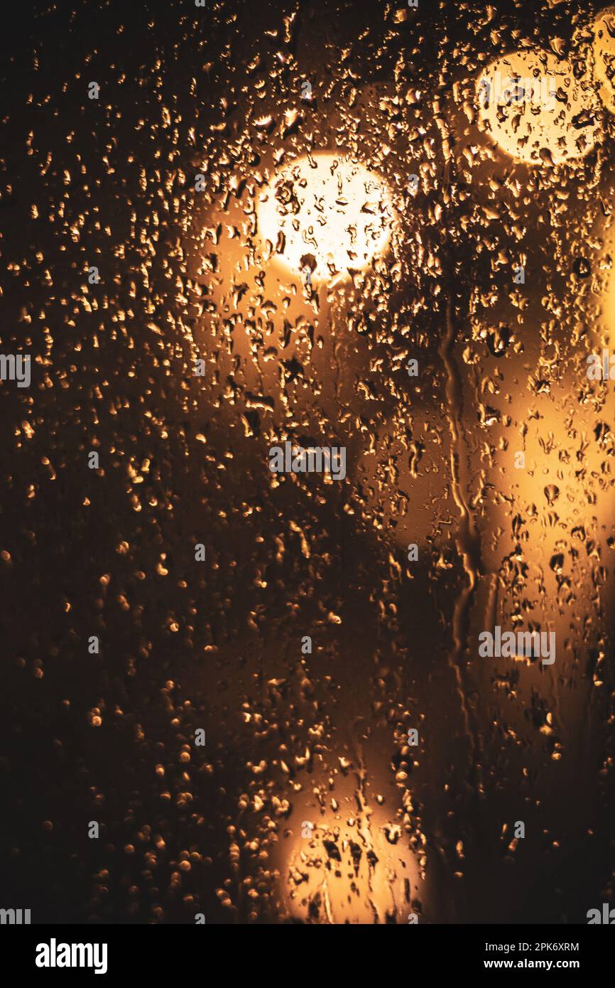 Surface en verre humide transparent avec gouttes d'eau contre les lumières de bokeh brillantes en soirée sombre Banque D'Images