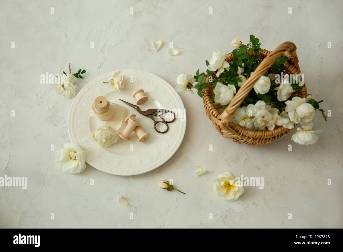 Ciseaux, ruban de soie, fleurs blanches et un panier de fleurs blanches sur un fond clair, image plate. nature morte avec des roses Banque D'Images