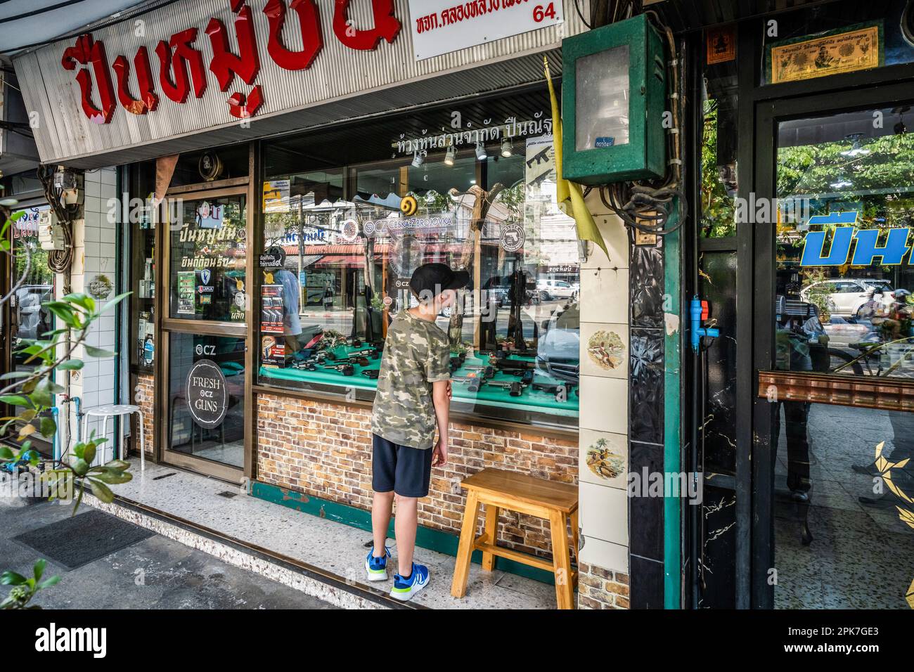 Un jeune touriste regarde à travers la fenêtre d'un magasin d'armes à feu montrant ses différents modèles à vendre, dans la vieille ville de Rattanakosin, un quartier populaire autour de Chinatown, à Bangkok, bien connu pour son marché d'armes à feu. La Thaïlande, largement connue comme une destination touristique accueillante, est également un pays inondé d'armes à feu faciles à obtenir, avec le plus grand nombre d'armes à feu dans les mains civiles en Asie du Sud-est et le plus haut taux de meurtres par arme à feu en Asie, avec un marché florissant d'armes à feu grises et noires. (Photo de Nathalie Jamois/SOPA Images/Sipa USA) Banque D'Images