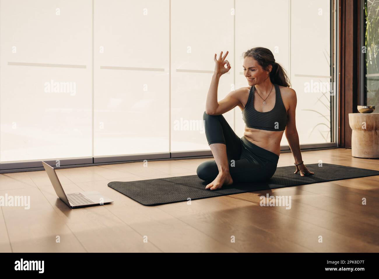 Femme âgée gaie faisant un geste ok pendant un cours de yoga en ligne. Bonne femme suivant un didacticiel de fitness virtuel sur un ordinateur portable. Femme mature prac Banque D'Images