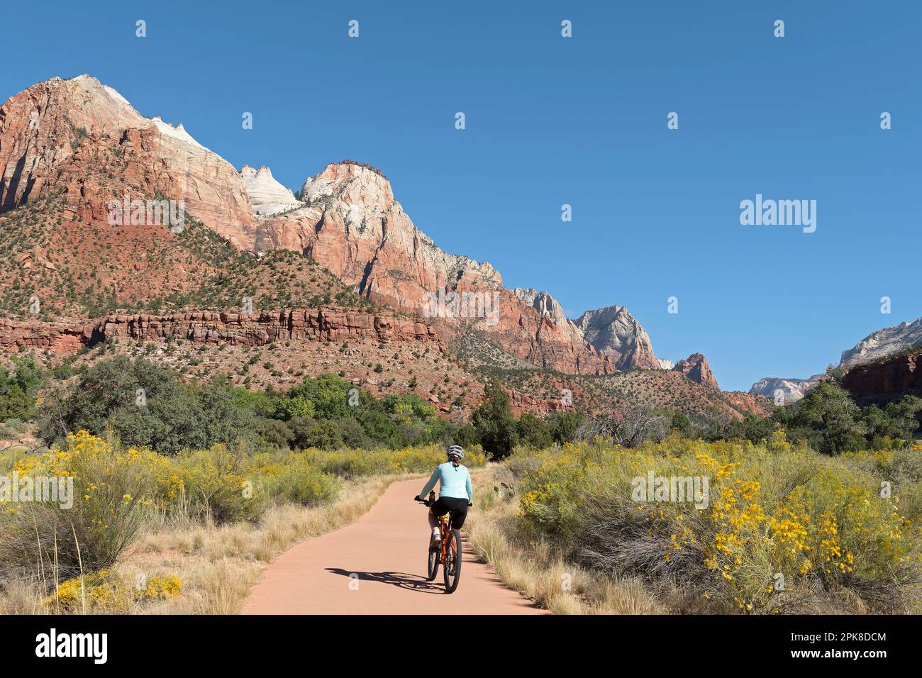 Une jeune femme qui fait du vélo de montagne sur le chemin Pa’rus Trail, un sentier pavé et facile au pied des montagnes abruptes du canyon de Zion, par une journée d'automne claire et ensoleillée Banque D'Images