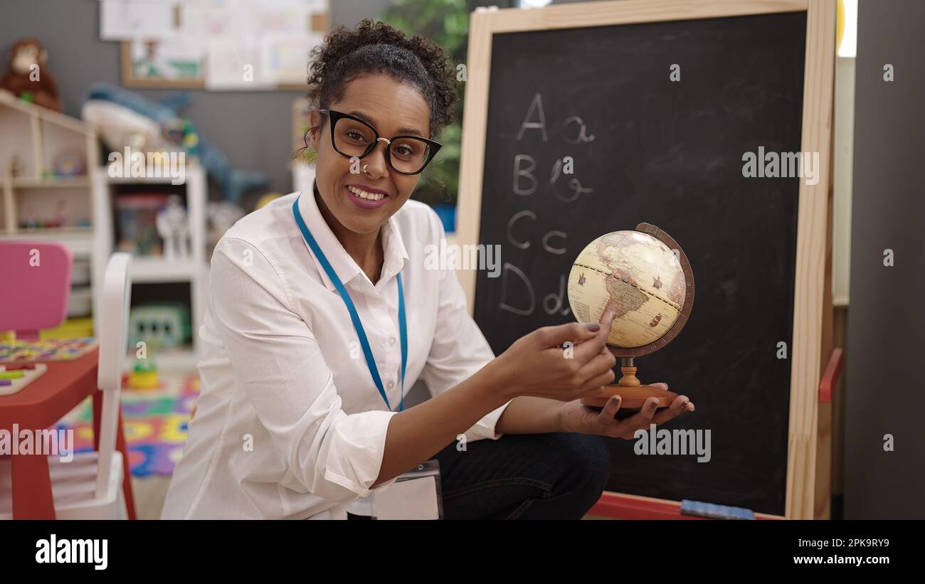 Femme enseignante afro-américaine souriante et confiante, tenant la terre à la maternelle Banque D'Images