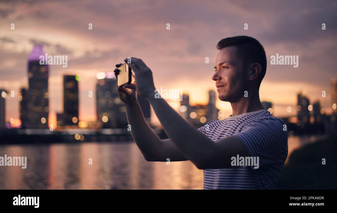 Homme qui prend des photos avec un smartphone d'horizon urbain. Ville moderne au beau coucher du soleil, Singapour. Banque D'Images