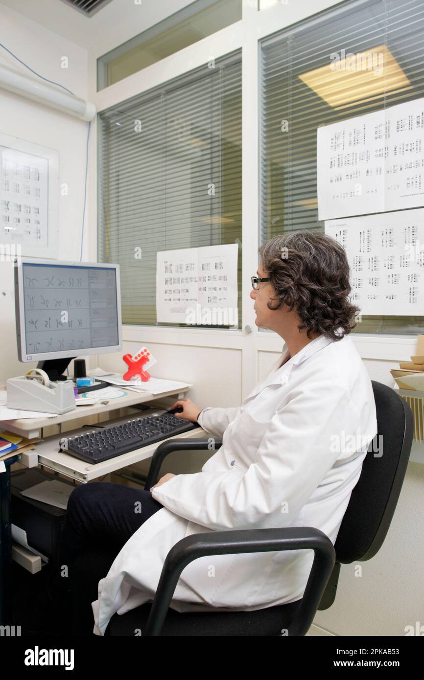 Laboratoire de cytogénétique, entouré de caryotypes, un médecin analyse les résultats d'un échantillon afin de rédiger un rapport. Banque D'Images