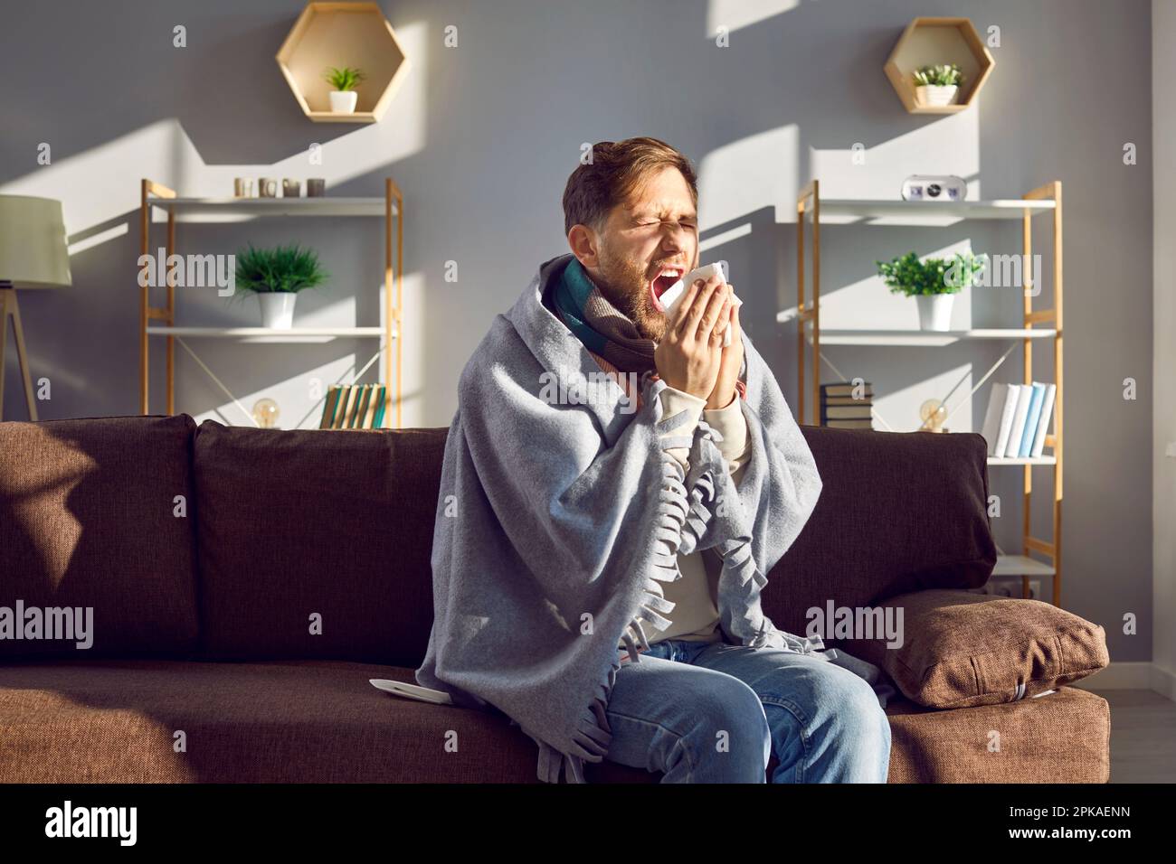 Jeune homme malade enveloppé dans une couverture éternuant et toussant Banque D'Images