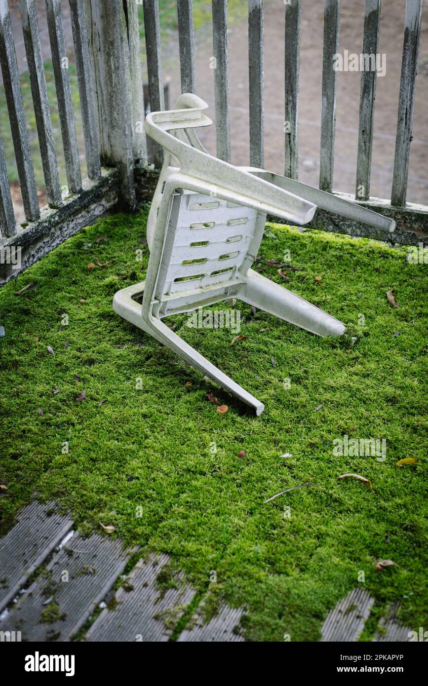 Chaise en plastique tombée sur un sol en teck de mousse d'un balcon Banque D'Images
