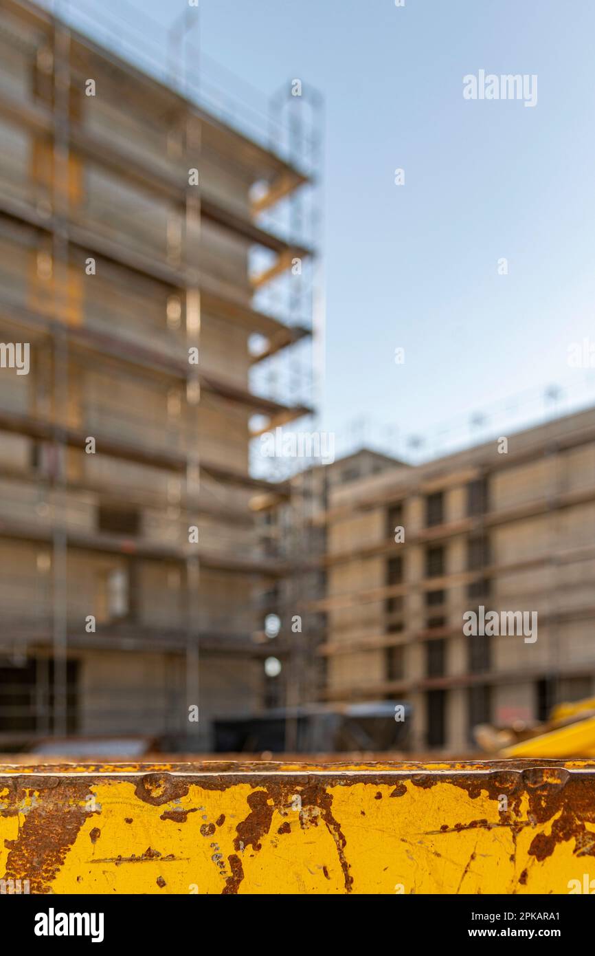 Conteneur jaune pour les supports de déchets de construction devant la coque de construction d'échafaudage avec ciel bleu au coucher du soleil Banque D'Images