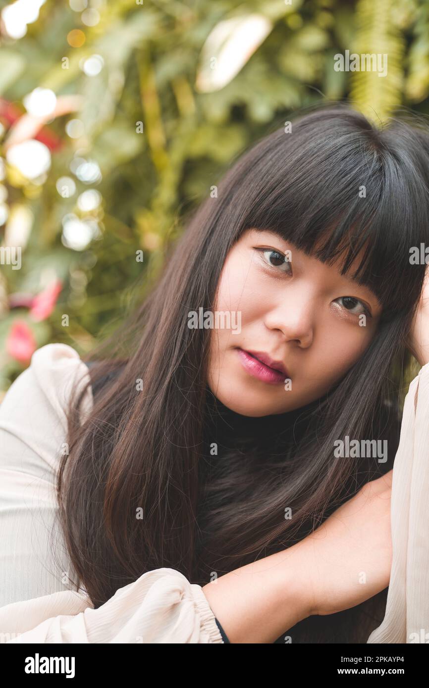 Gros plan de la jeune femme asiatique dans un jardin | tons bruns chauds | cheveux longs Bangs | mains cadrage visage Banque D'Images