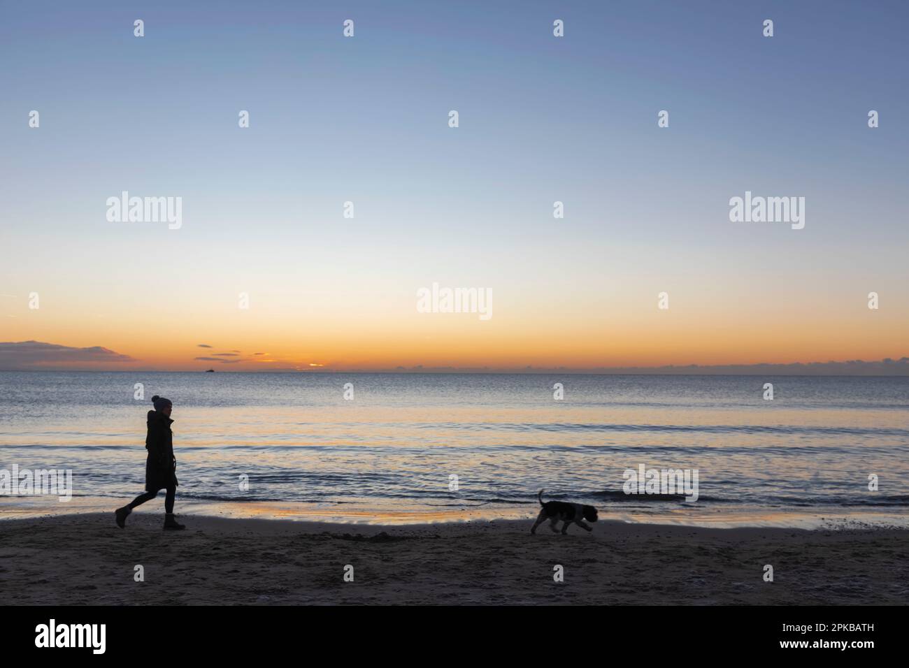 Angleterre, Dorset, Poole, Sandbanks Beach, Silhouette of Woman Walking Dog at Sunrise Banque D'Images
