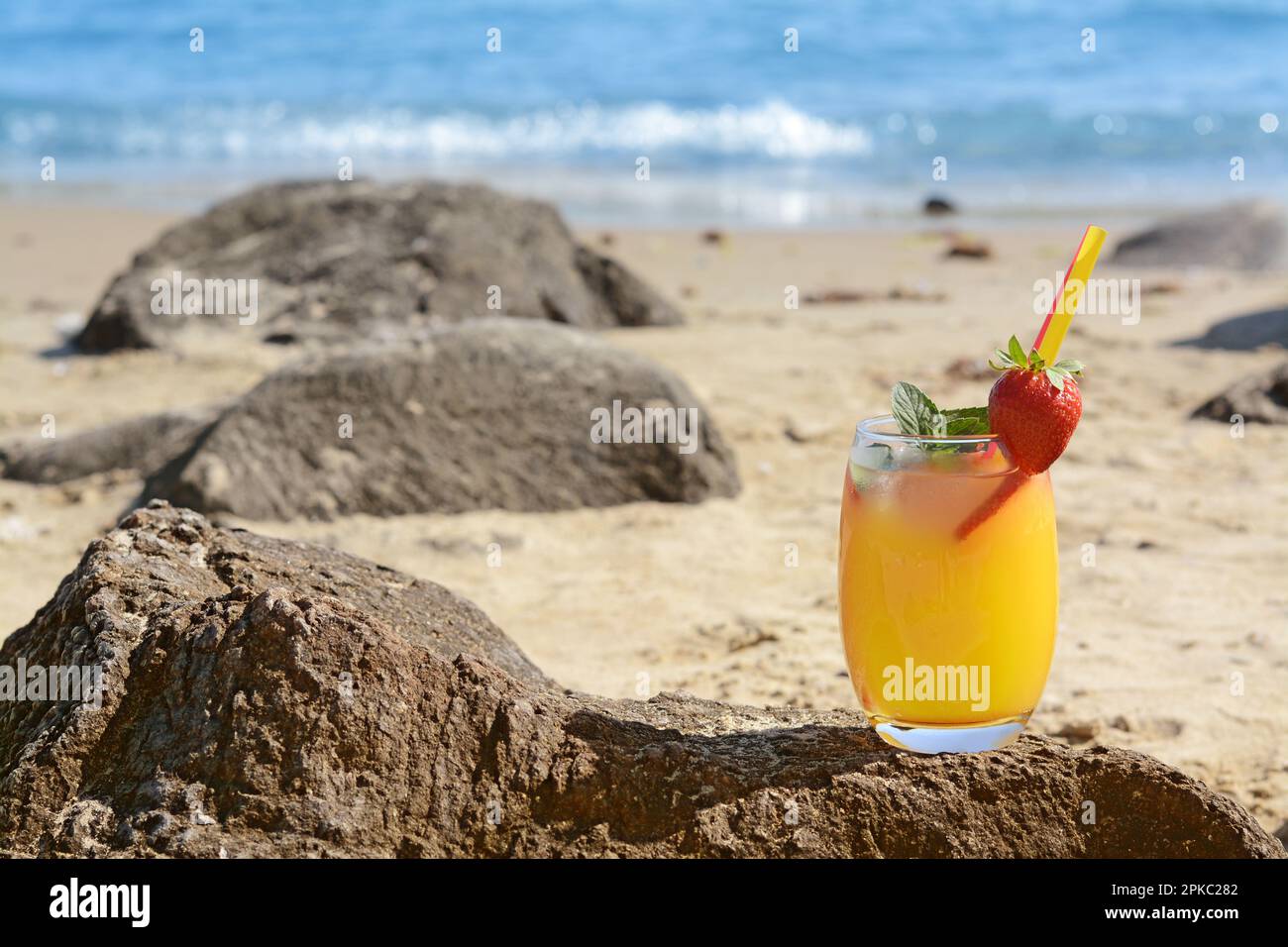 Verre de boisson rafraîchissante avec fraise sur la plage près de la mer, espace pour le texte Banque D'Images