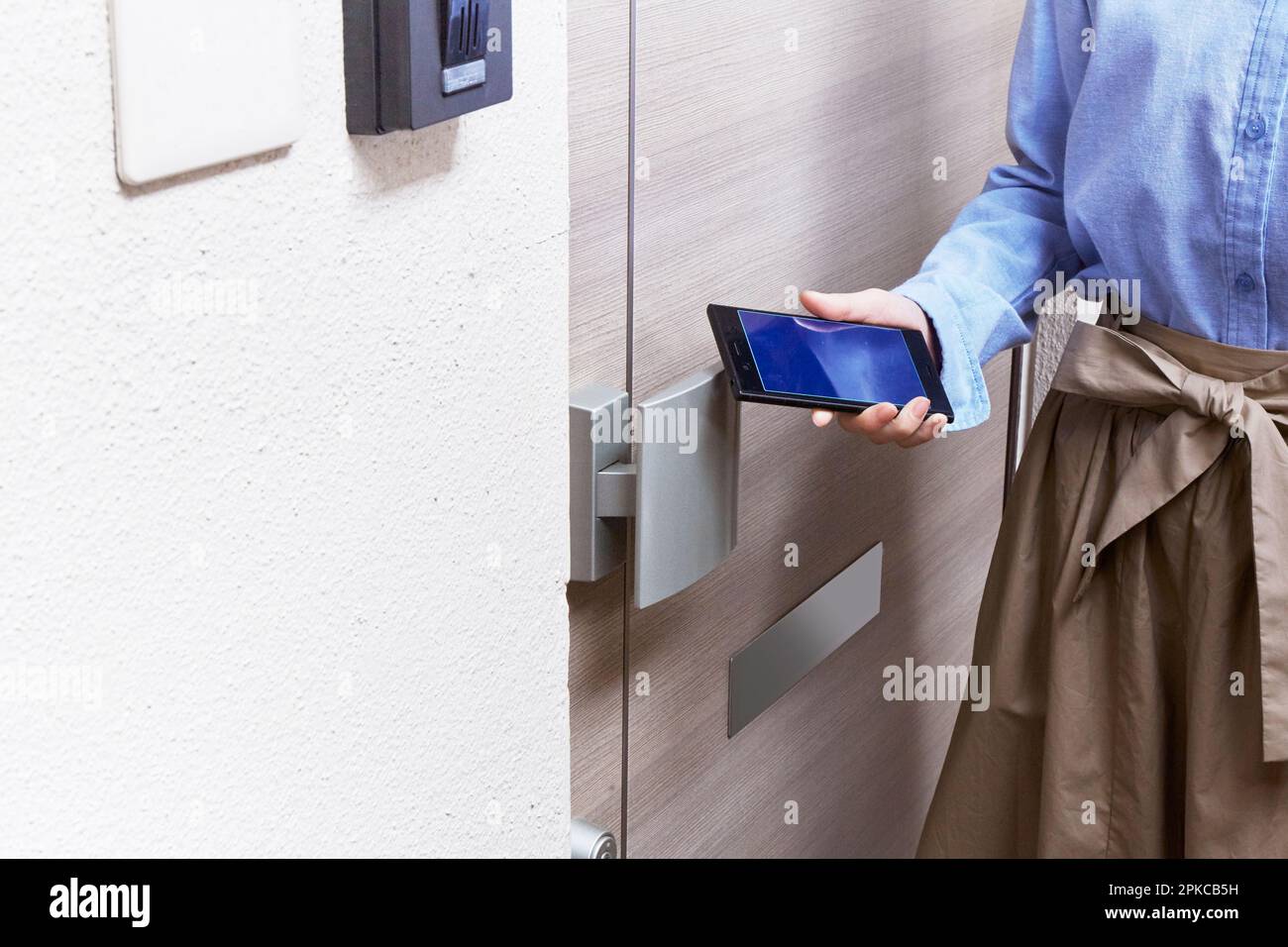 Femme tenant un smartphone par-dessus la porte avant Banque D'Images