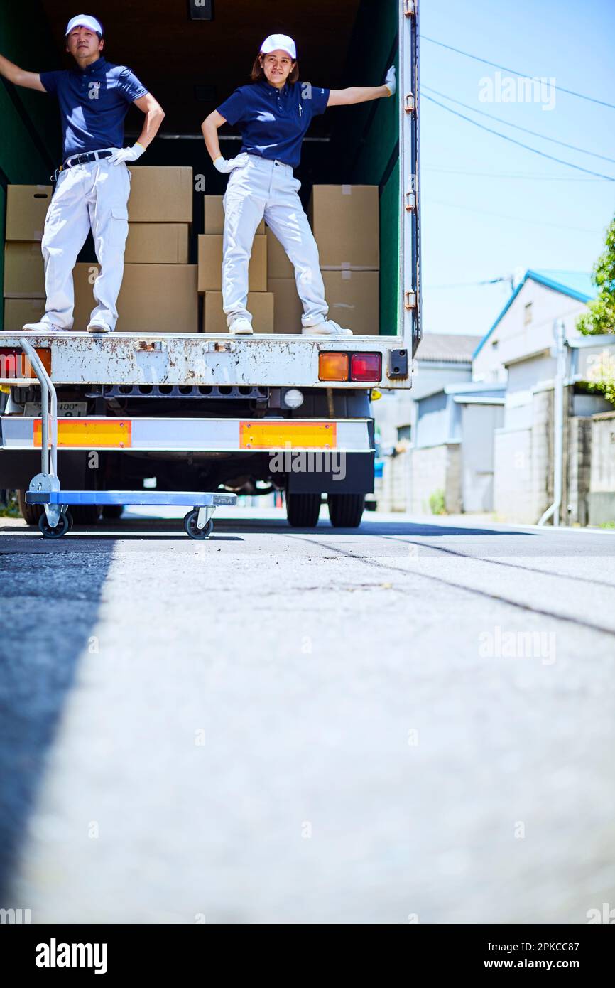 Homme et femme en vêtements de travail posant à l'arrière d'un camion dans la rue Banque D'Images