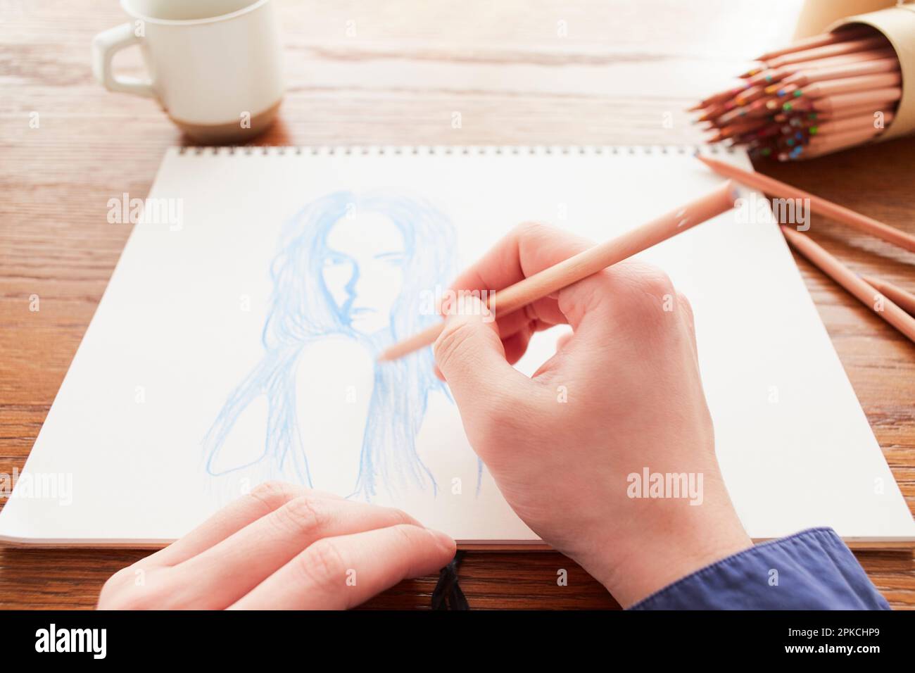 Homme dessinant une photo d'une femme dans un carnet de croquis sur une table Banque D'Images