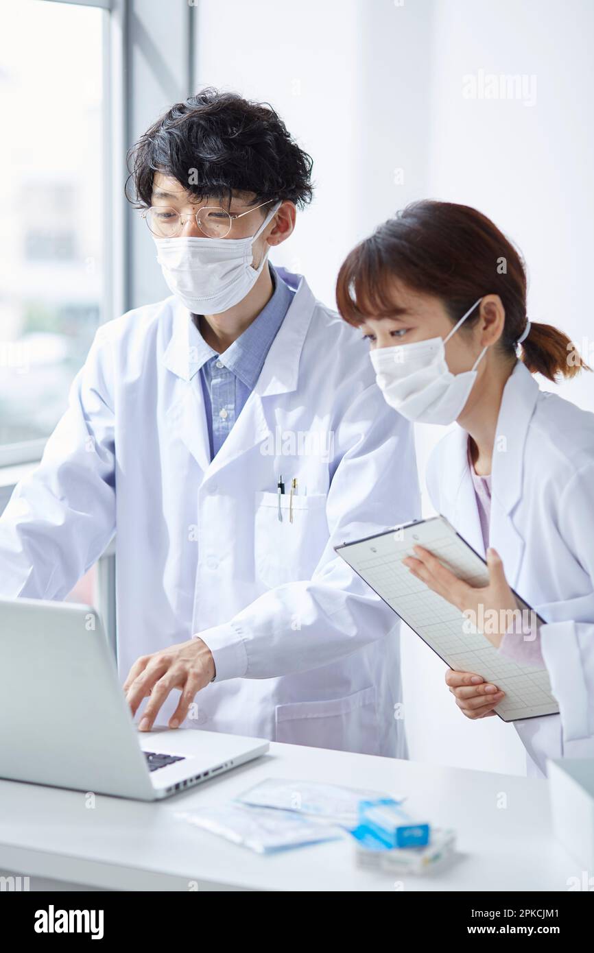 Homme et femme en blanc vérifiant la médecine tout en regardant l'ordinateur portable Banque D'Images