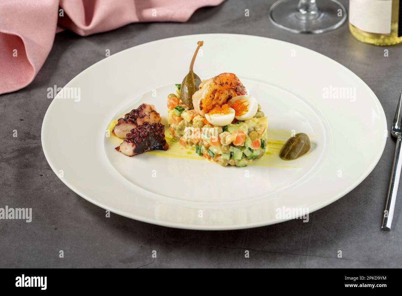 Salade russe à la sauce aioli, crevettes, poulpes et câpres sur une assiette en porcelaine blanche Banque D'Images