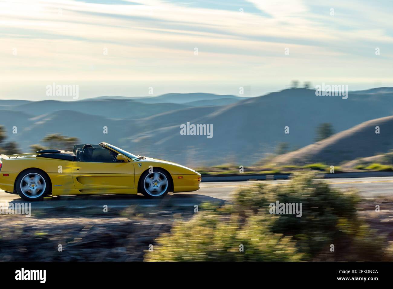 Une voiture de sport jaune voyageant le long d'une route sinueuse avec des montagnes majestueuses en arrière-plan. Banque D'Images