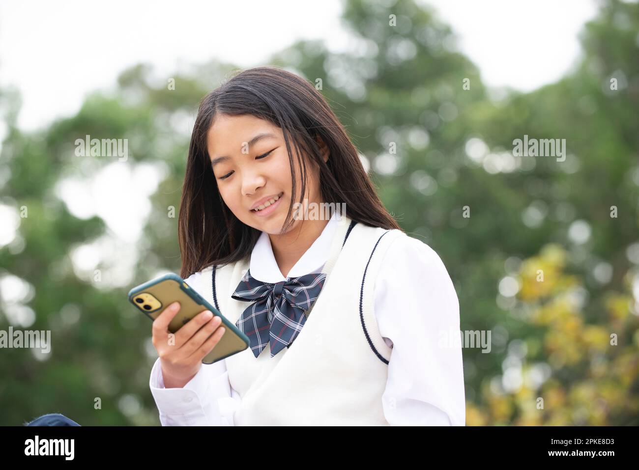 Une étudiante en uniforme scolaire regardant son téléphone Banque D'Images