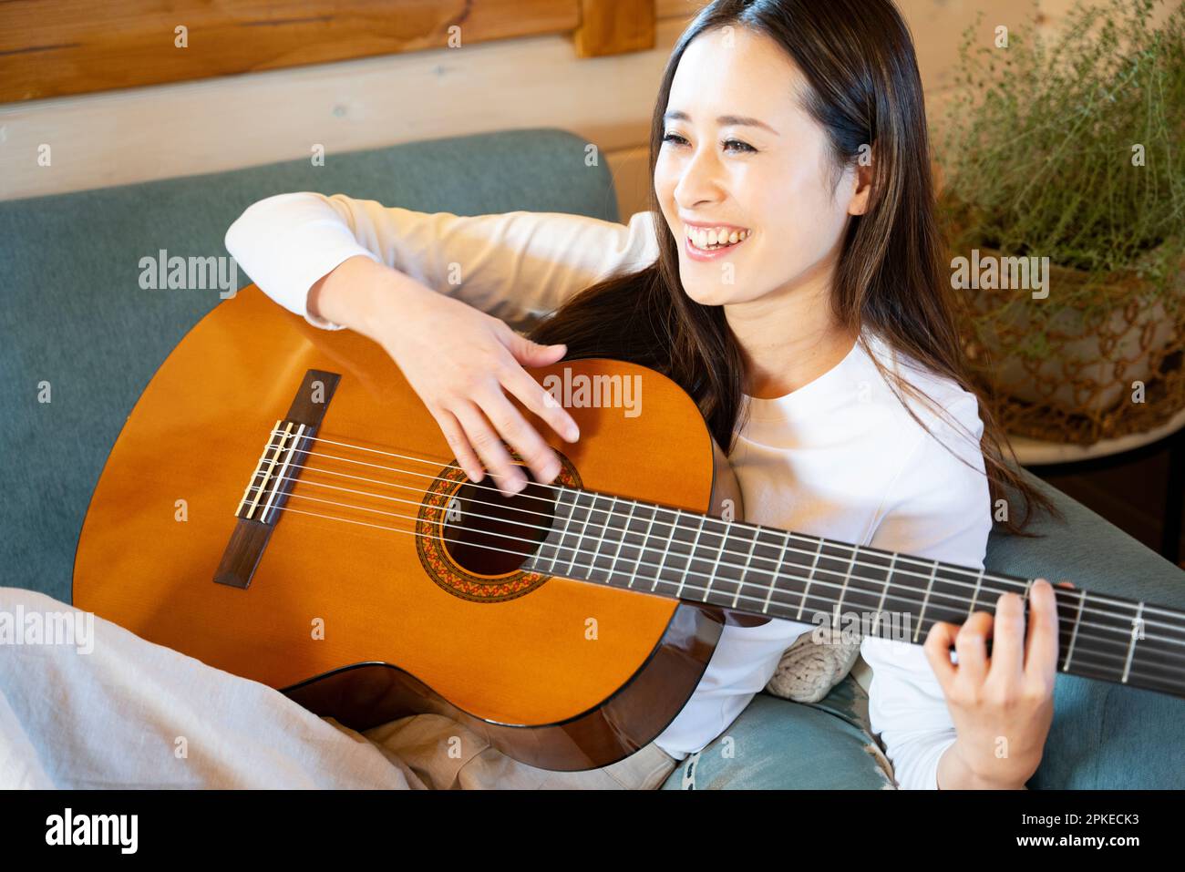 Femme jouant de la guitare sur un canapé Banque D'Images