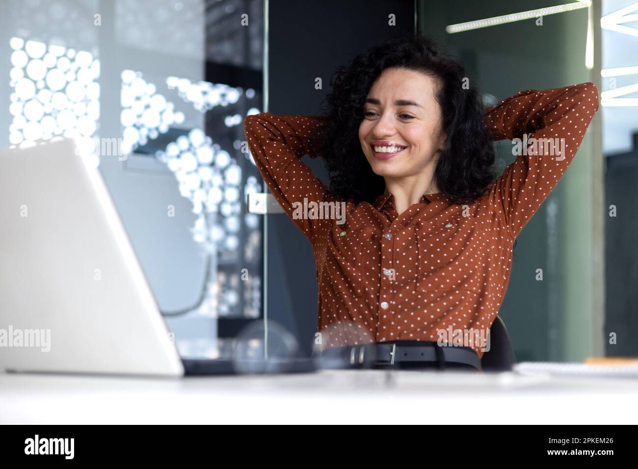 Une femme qui pense bien au travail au bureau, une femme d'affaires qui a les mains derrière la tête a bien terminé son travail, une femme latino-américaine satisfaite des résultats obtenus en regardant l'écran d'un ordinateur portable. Banque D'Images