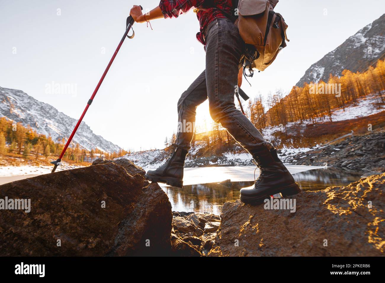 Une jeune fille marche avec un sac à dos et des bâtons de randonnée contre le lac de montagne et le coucher du soleil Banque D'Images