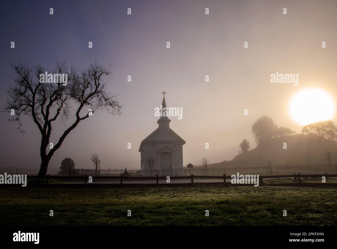 Soleil lumineux et brouillard sombre sur petite église et arbre dans la campagne rurale à l'aube Banque D'Images