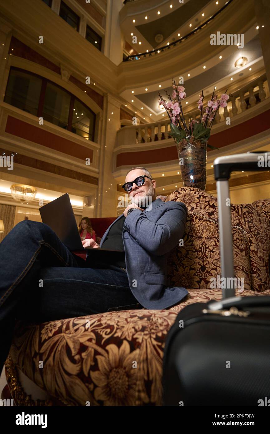 Imposant homme assis avec un ordinateur portable sur un canapé en velours Banque D'Images