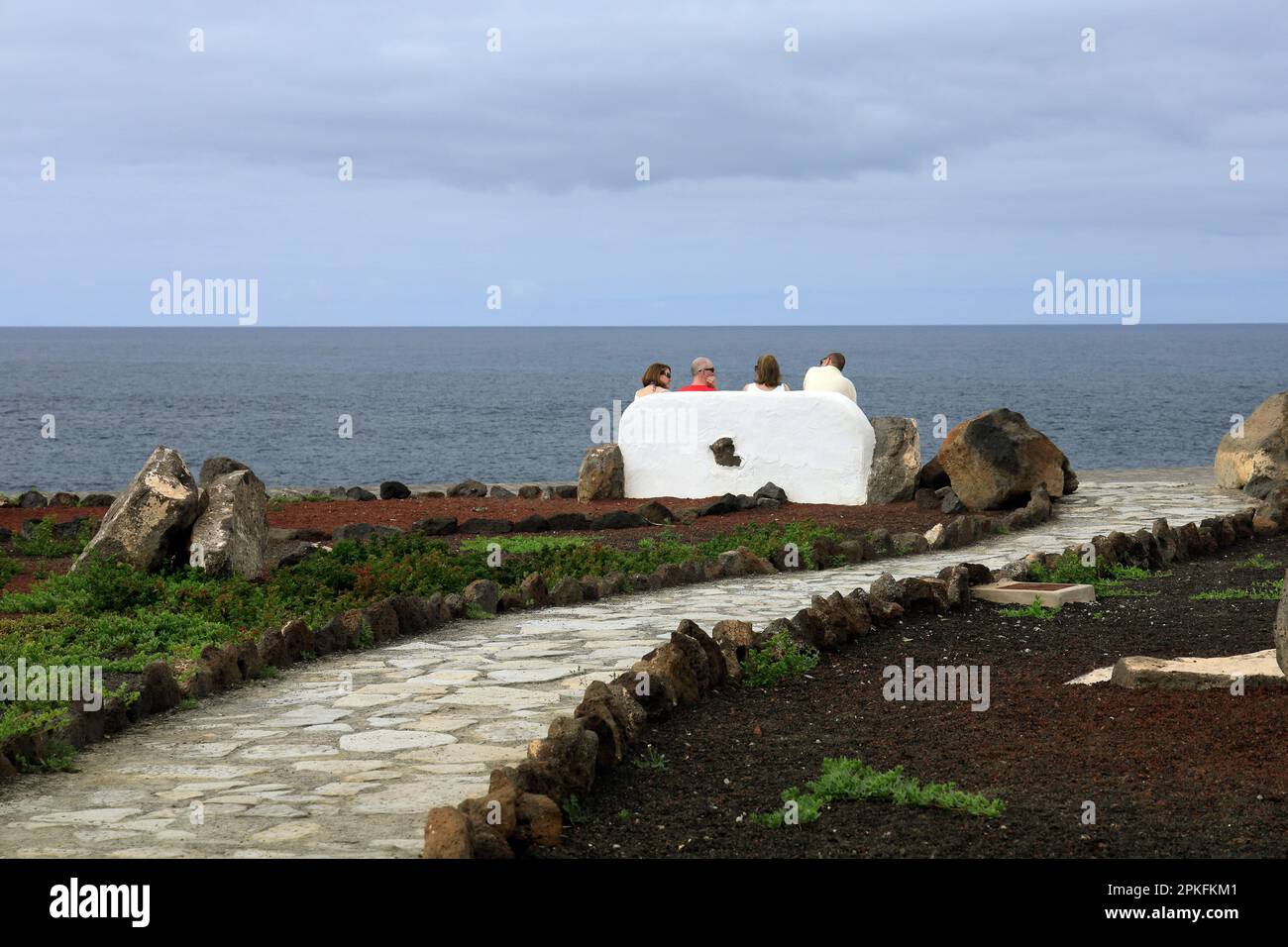 Quatre personnes assises sur un banc de pierre donnant sur l'océan Atlantique près du phare de Faro de Pechiguera, Lanzarote. Prise février / Banque D'Images