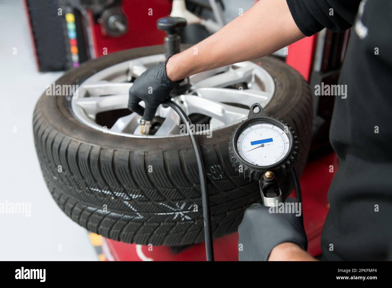 Un ouvrier agricole de service de garage pompant un pneu automobile équilibré à l'aide d'un manomètre dans un atelier automobile Banque D'Images