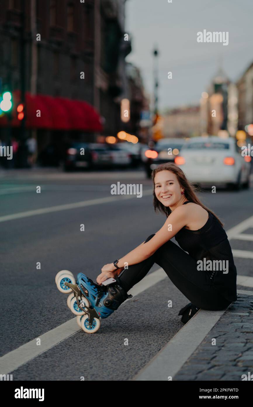 Photo extérieure d'une femme active mince pose sur l'asphalte met sur les rollerskates être de bonne humeur passe du temps libre à monter des rollerbdes en milieu urbain. Bloure Banque D'Images