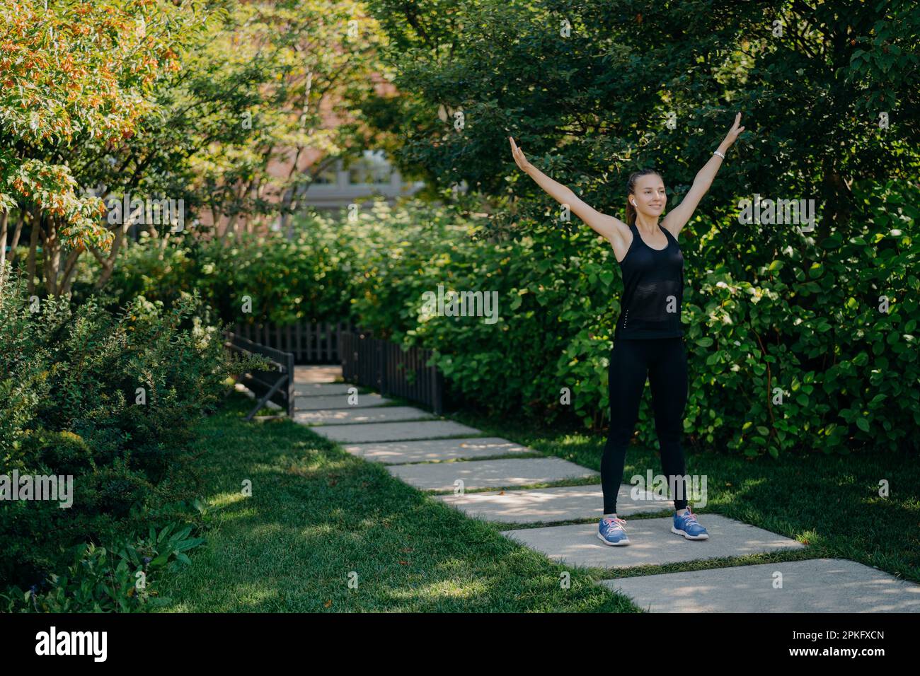 Prise de vue en longueur de active sportswoman lève les bras respire profondément habillé en tenue active a entraînement sportif dans le parc pendant l'heure du matin écoute de la musique Banque D'Images