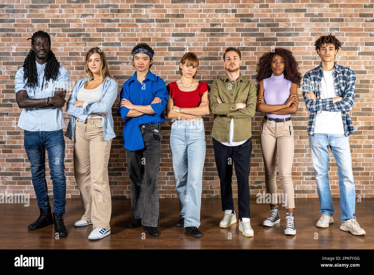Groupe de jeunes posant devant un mur de briques, expressions sérieuses et décisives Banque D'Images