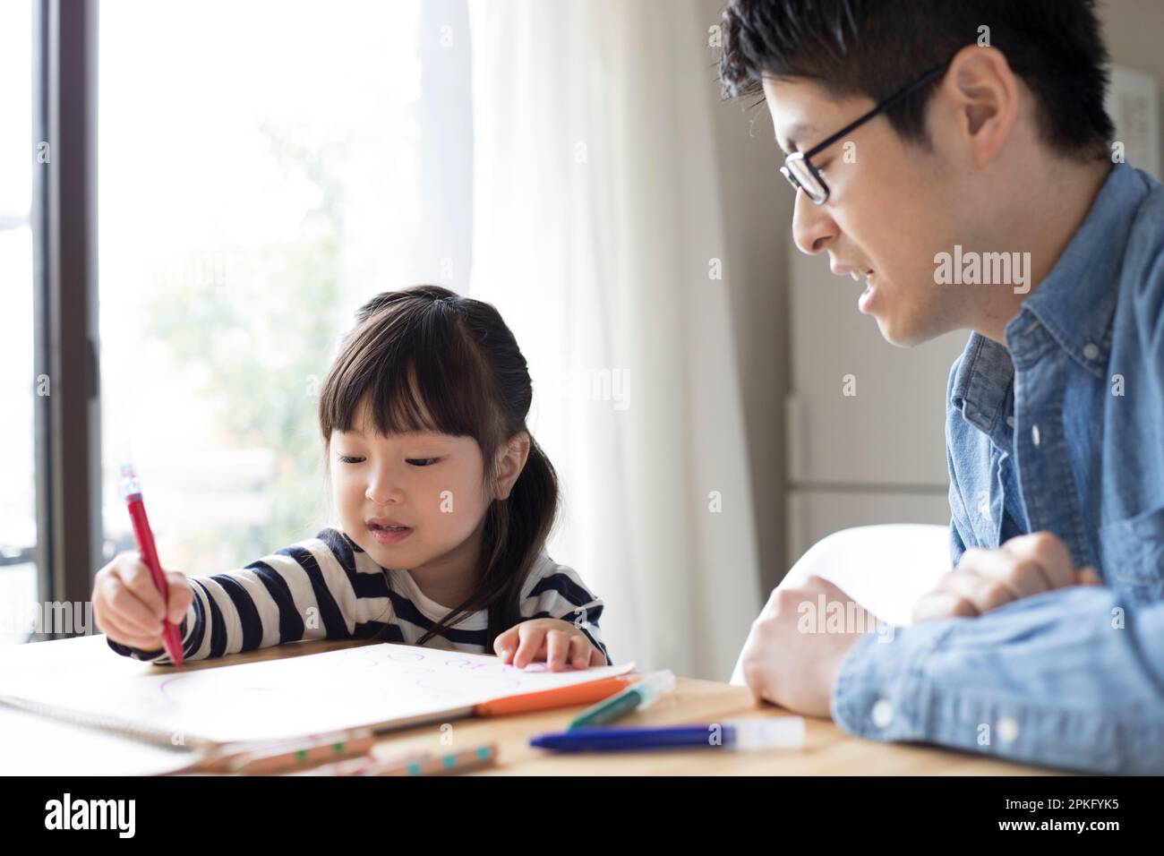 Fille dessin dans son carnet de croquis avec son père regardant au-dessus d'elle Banque D'Images