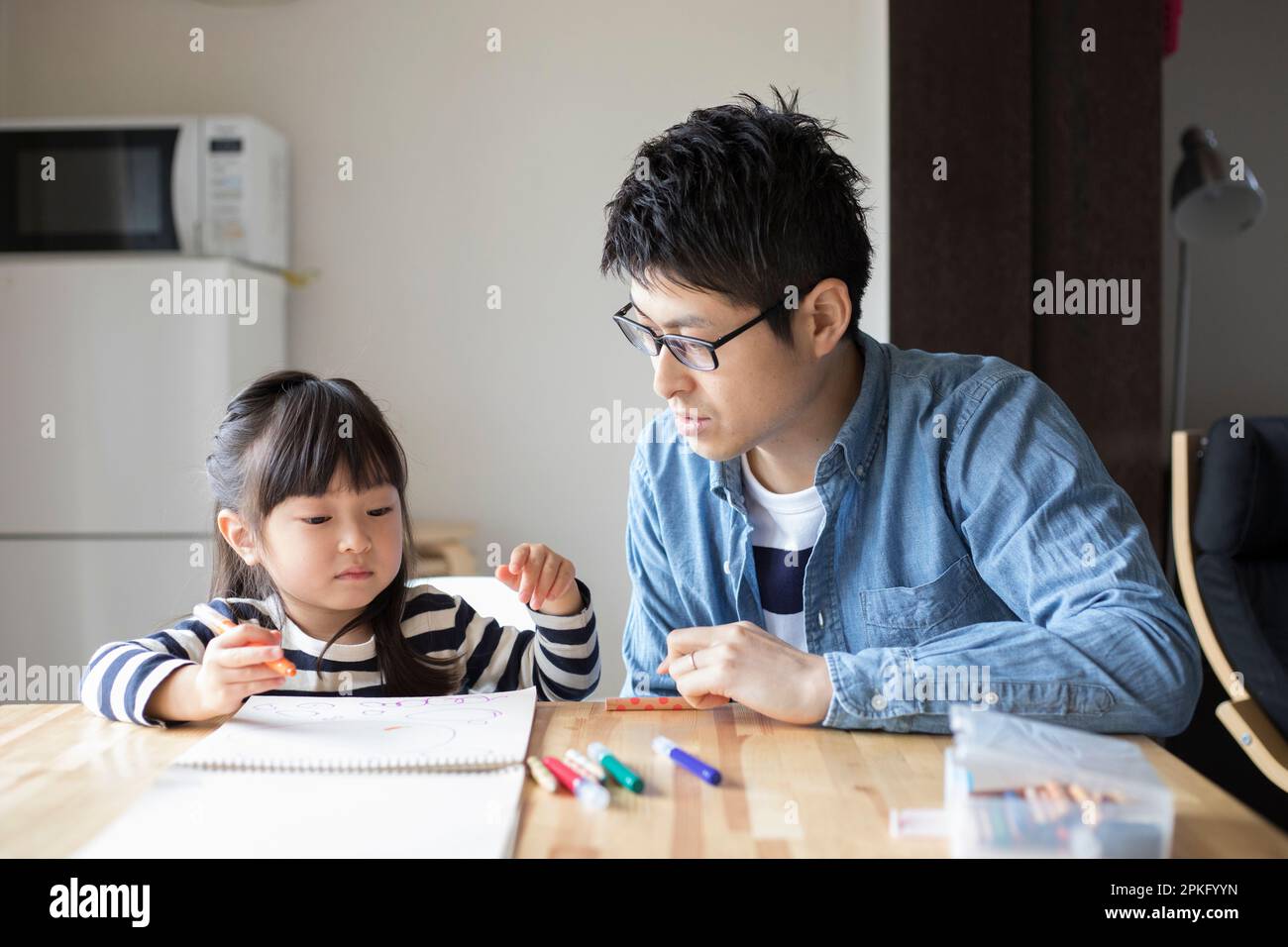 Fille dessin dans son carnet de croquis avec son père regardant au-dessus d'elle Banque D'Images