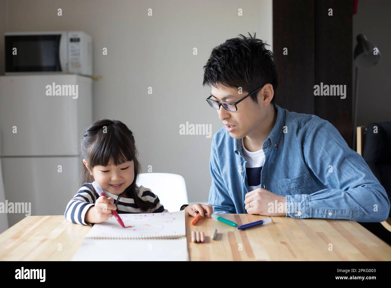 Fille dessin dans son carnet de croquis et son père regardant au-dessus d'elle Banque D'Images