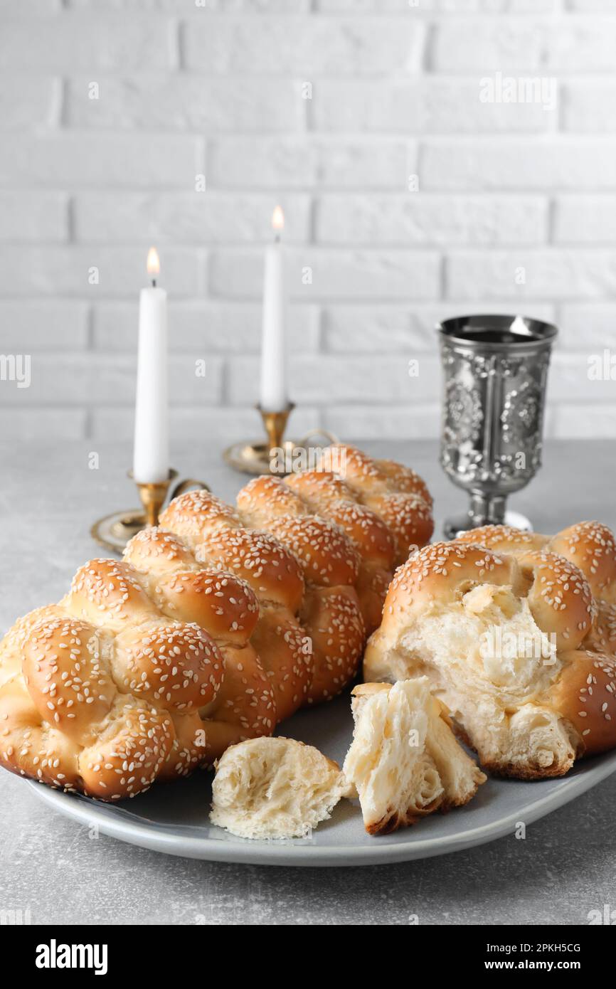 Pain tressé fait maison avec graines de sésame, gobelet et bougies sur table grise, gros plan. Challah traditionnel de Shabbat Banque D'Images