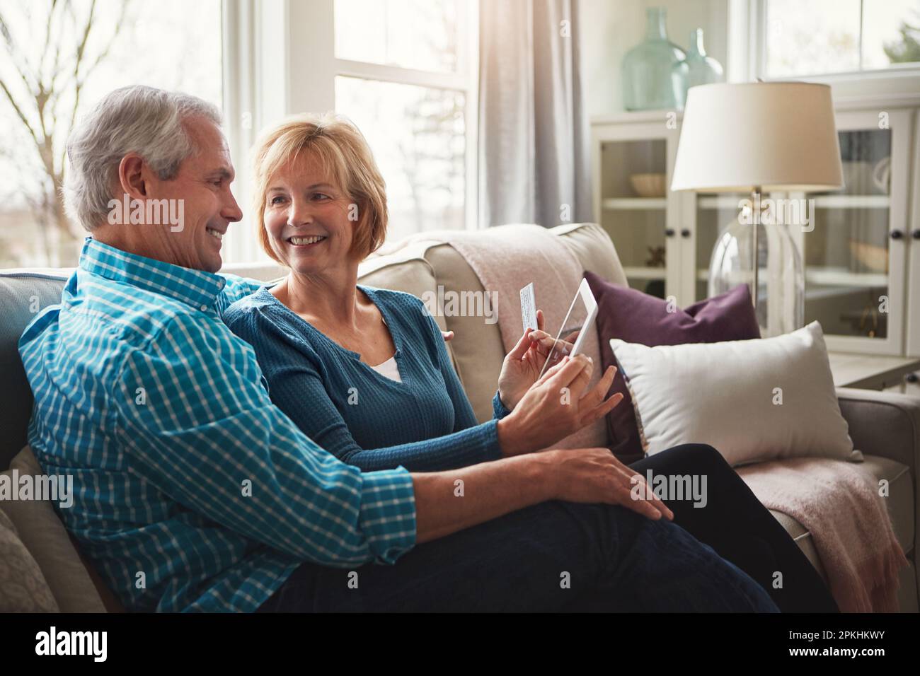Confort, commodité et crédit combinés. un heureux couple mature se relaxant sur le canapé et utilisant une tablette numérique et une carte de crédit ensemble. Banque D'Images