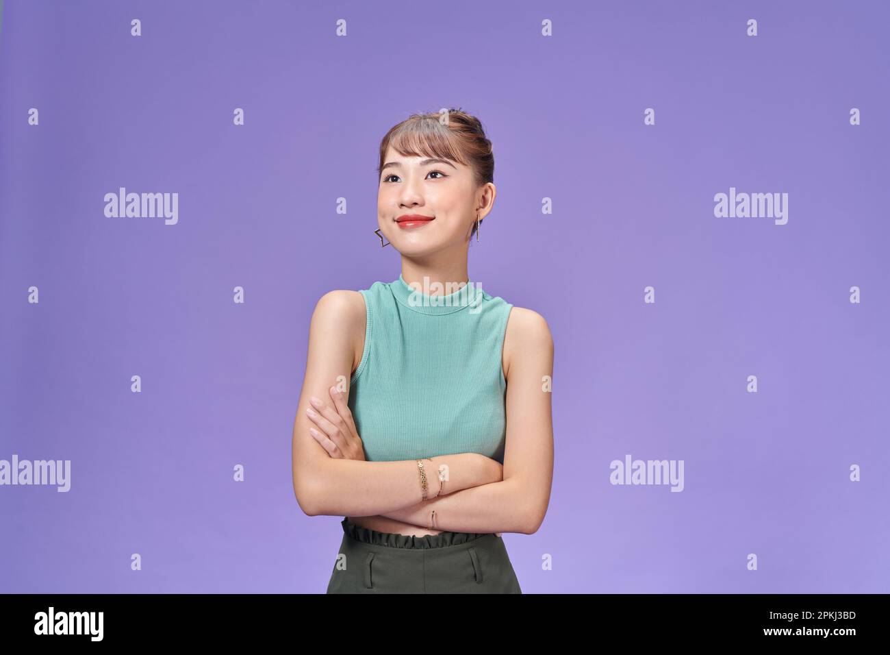 Femme asiatique confiante et élégante croiser les bras sur la poitrine et souriante, debout sur fond violet Banque D'Images