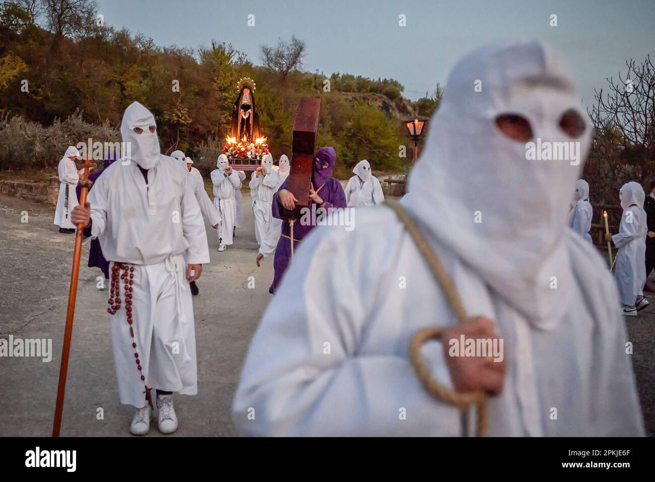 Un pénitent de la Fraternité de la 'Santa de la Vera Cruz' porte une croix de Jésus Christ, tandis que derrière lui plusieurs pénitents portent la Dolorosa en procession à travers les rues de Torres del Río, Navarre, Espagne. La Fraternité de la 'Santa de la Vera Cruz' célèbre une procession caractéristique de la semaine Sainte à Torres del Río, Navarre, Espagne, dans laquelle les pénitents sont habillés en blanc, faisant une petite section du Camino de Santiago, dans laquelle ils portent une croix qu'un pénitent brise le silence de la nuit en battant au son des traces, tandis que d'autres membres de la fraternité Banque D'Images