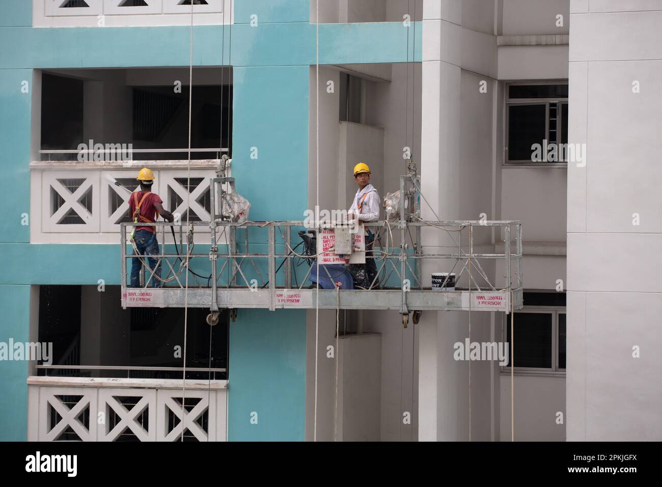 Deux travailleurs sur l'ascenseur de l'échafaudage, l'un travaillant à l'aide d'un jet d'eau pour nettoyer la saleté de l'extérieur du mur et l'autre contrôlant l'élévation de la hauteur. Banque D'Images