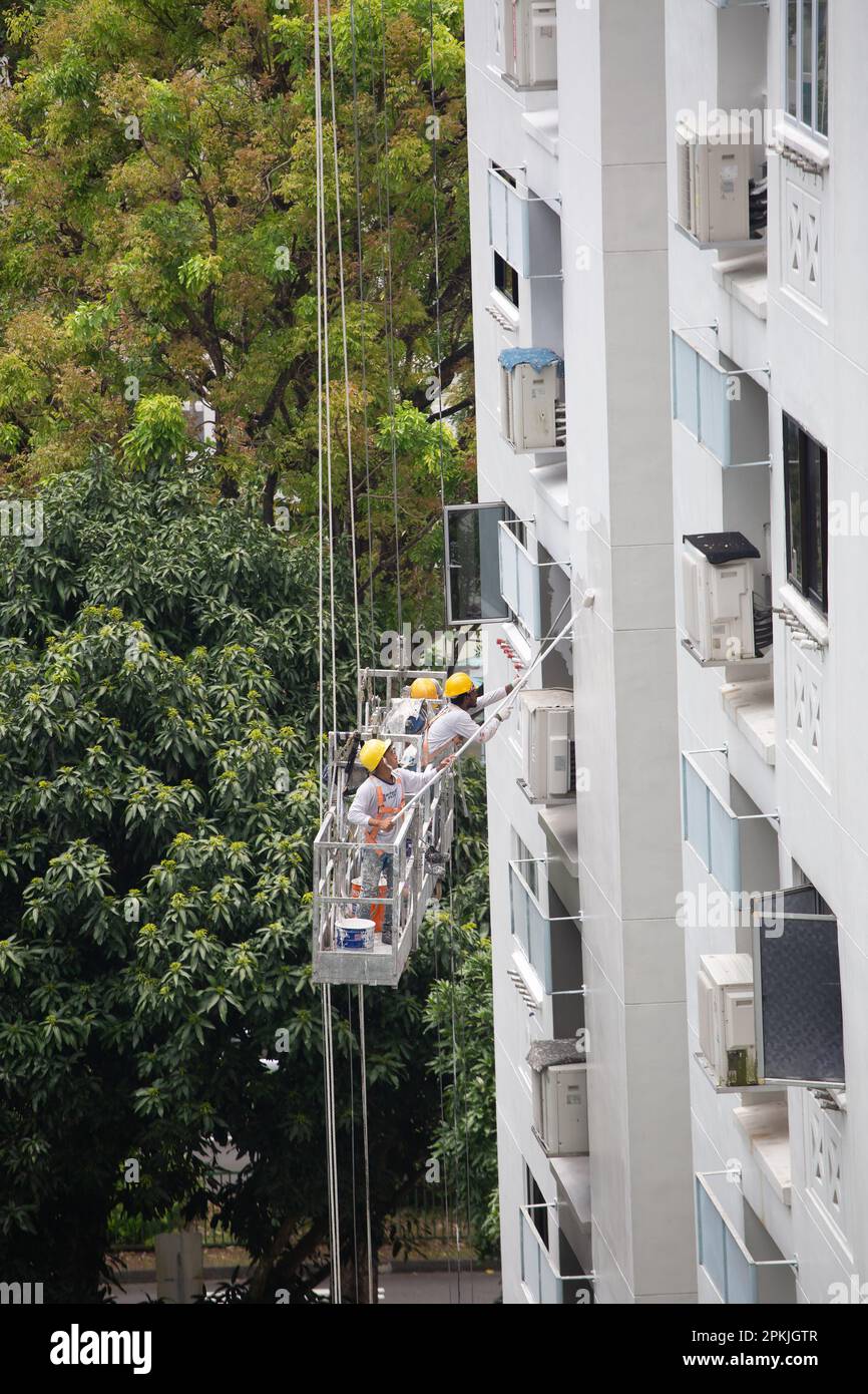 Vue verticale de trois spécialistes de la peinture dans un échafaudage d'ascenseur travaillant en hauteur pour peindre l'extérieur du mur du bâtiment HDB. Singapour. Banque D'Images