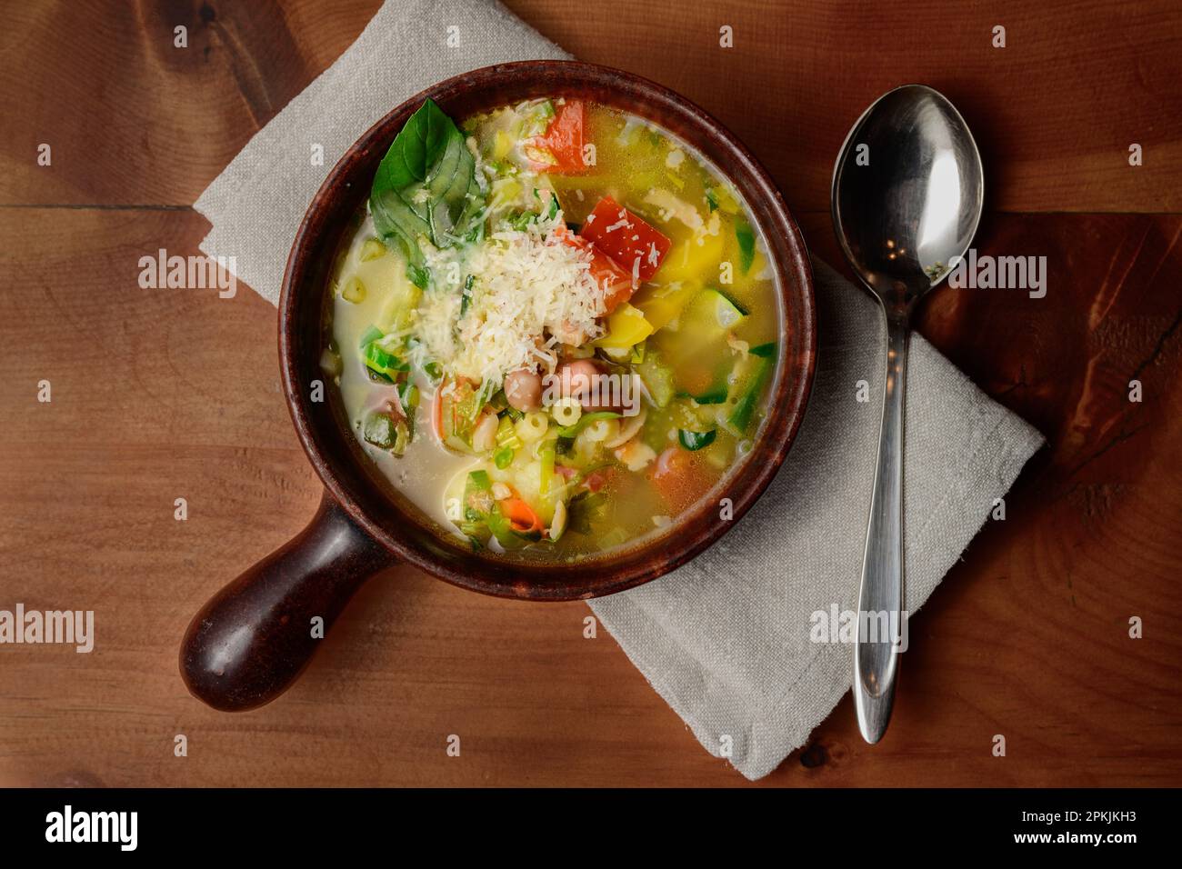 Soupe de légumes italienne minestrone aux haricots et aux pâtes dans un bol rustique en terre cuite avec cuillère et serviette de table Banque D'Images