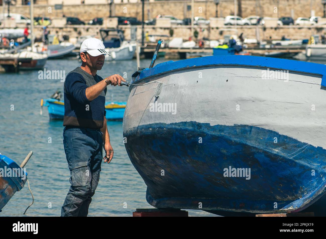 Pêcheur réparant et peignant un vieux bateau de pêche en bois au quai du port de Bari, Puglia Italie Banque D'Images