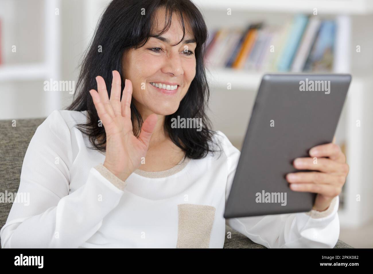 femme moderne d'âge moyen assise sur un canapé à la maison à l'aide d'une tablette Banque D'Images